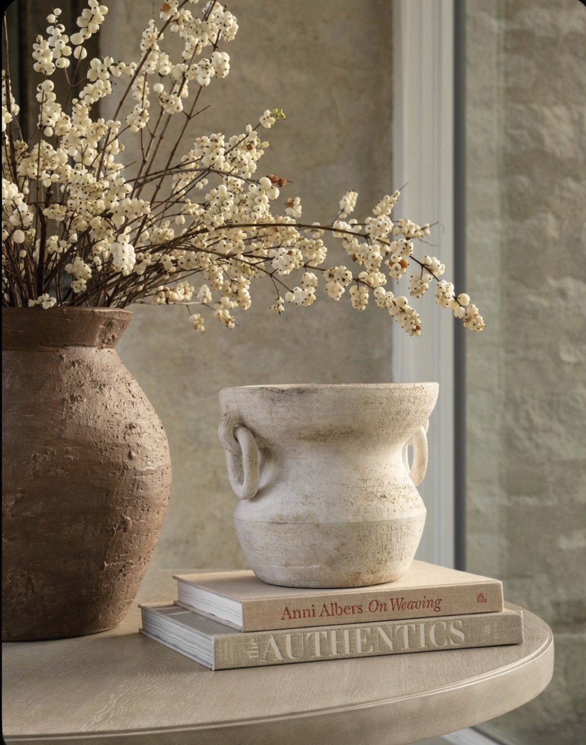 Textured ceramic vessels and soft white branches on a natural wood table