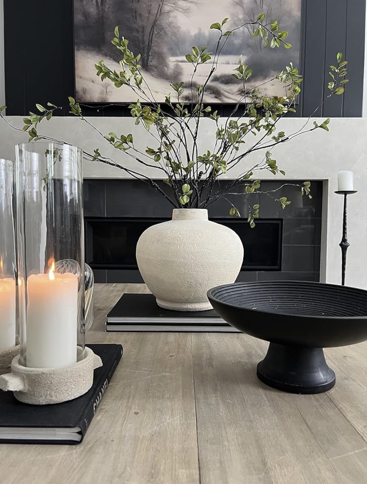 Styling inspiration with a cream vase, leafy branches, candlelight, and a black sculptural bowl